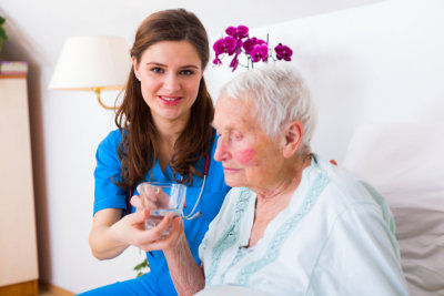 nurse helping sick elderly women to drink in bed in a nursing home